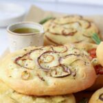 Baked sourdough focaccia rolls on parchment paper with a small dipping bowl of olive oil.