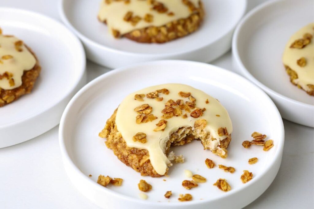 Close up of sourdough honey oat cookie on a plate with a bite taken out and additional cookies in the background.