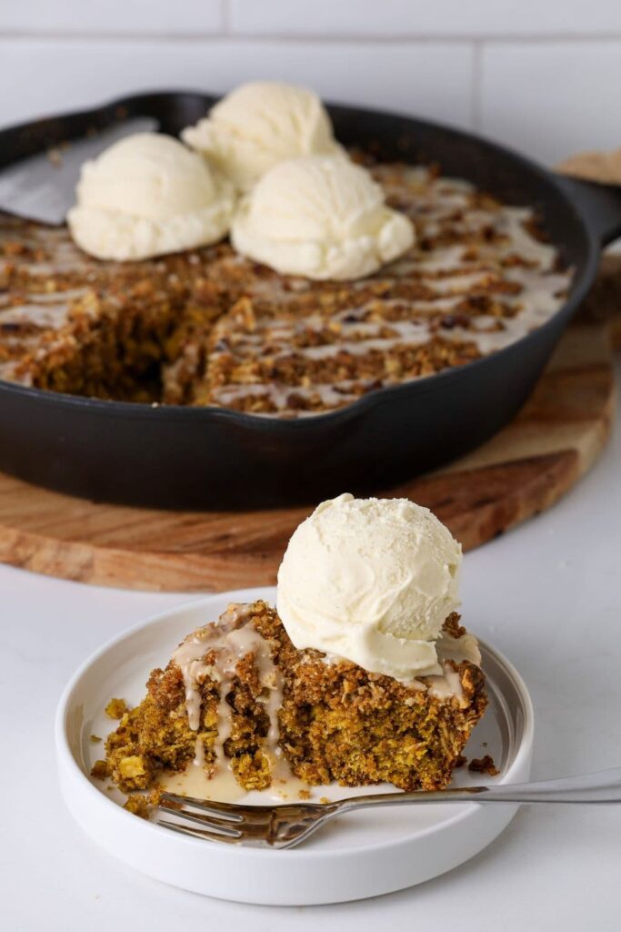 Slice of sourdough oatmeal pumpkin cookie skillet on a plate with a fork and a scoop of vanilla ice cream on top.
