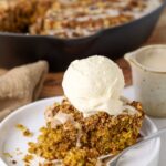 Close up of a slice of sourdough oatmeal pumpkin cookie skillet on a plate with a fork taking a bite and a scoop of vanilla ice cream on top.