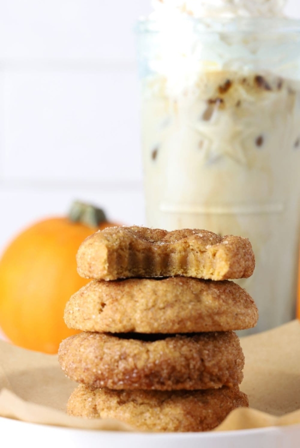 Four sourdough pumpkin snickerdoodle cookies stacked on parchment paper with a coffee drink in background.