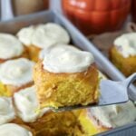 An image showing sourdough pumpkin sourdough rolls wtih cream cheese frosting with one being lifted up with a slice.