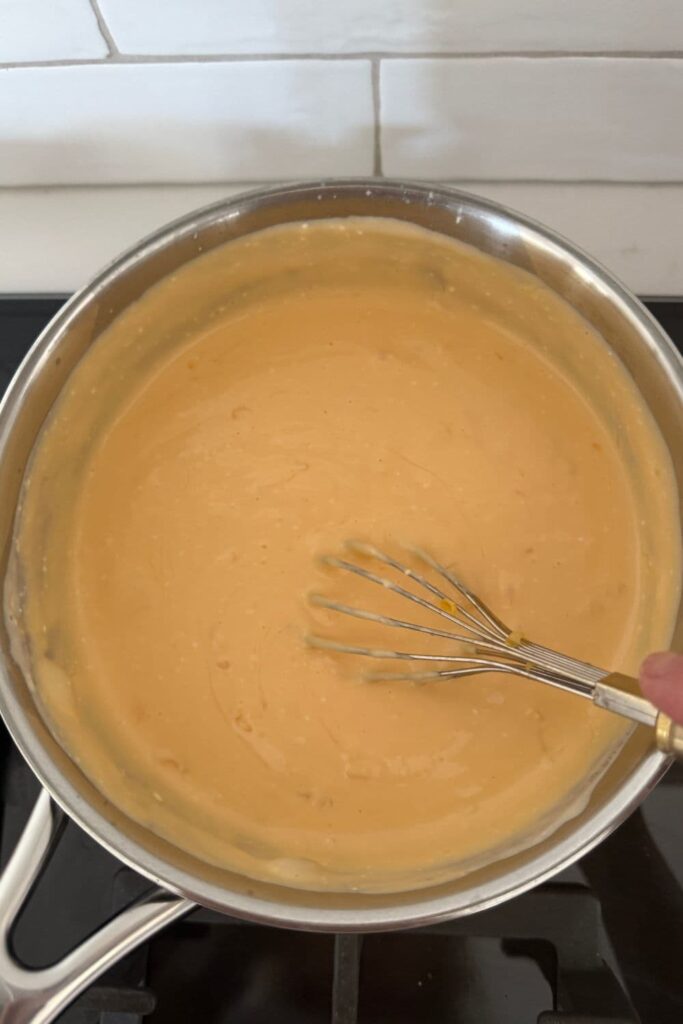 A saucepan of beer cheese dip that has all three ingredients added and is being whisked until smooth.