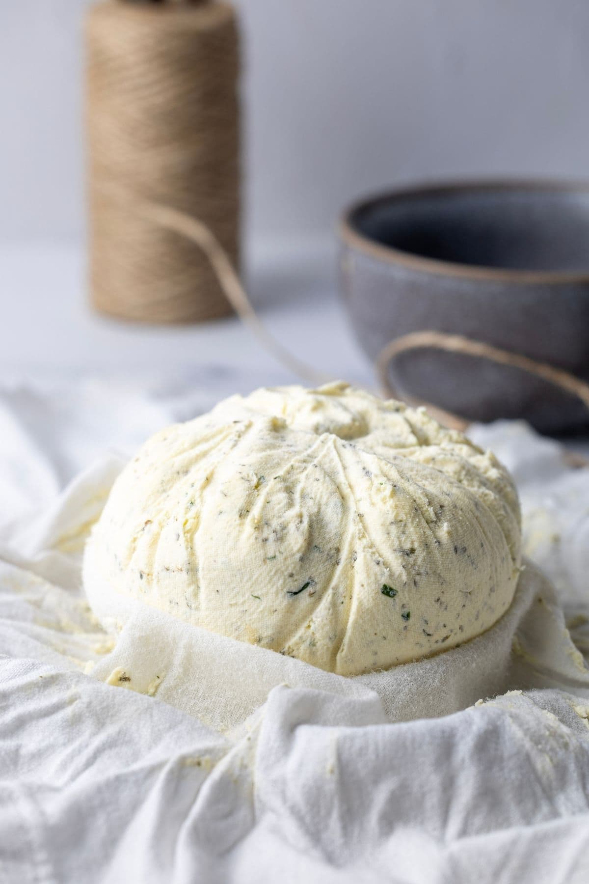 A round of homemade Boursin cheese that has been unwrapped from the cloth to show the round shape.
