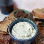 A small blue bowl containing homemade boursin cheese. The bowl is part of a charcuterie board with apple, sourdough bread and lavosh crackers.