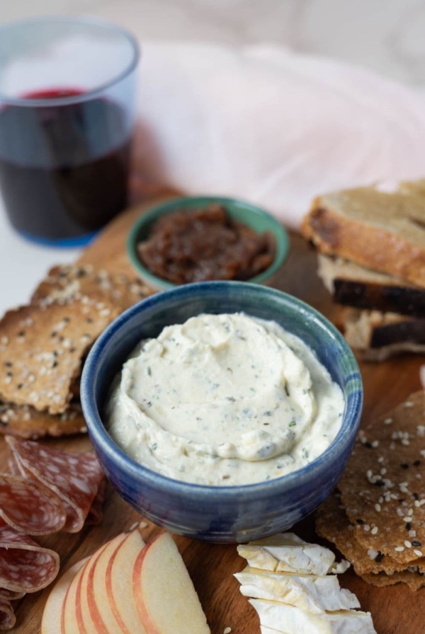 A small blue bowl containing homemade boursin cheese. The bowl is part of a charcuterie board with apple, sourdough bread and lavosh crackers.