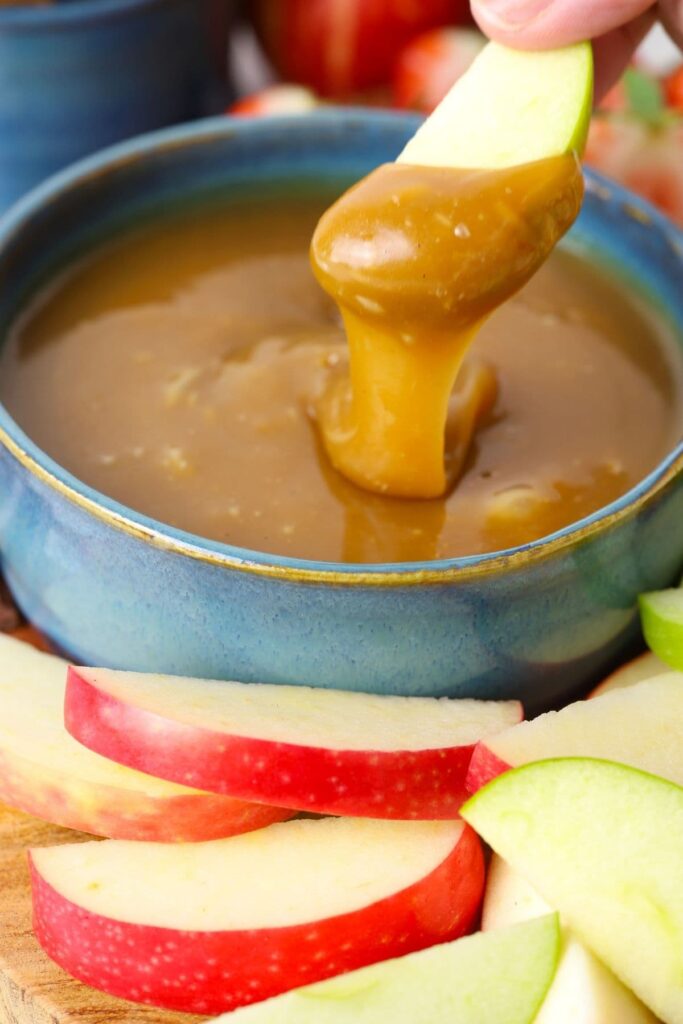 Dipping an apple into the homemade caramel dip to show the texture and how the dip stays on the apple slice.