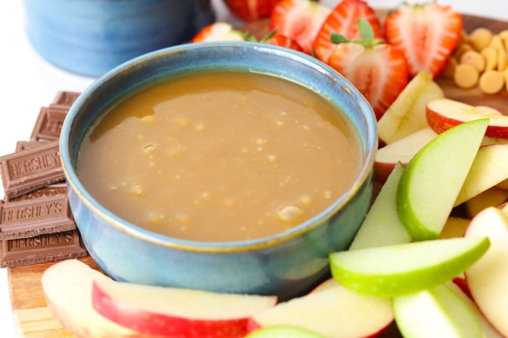 A bowl of homemade caramel dip on a serving platter with strawberries, apples and chocolate.