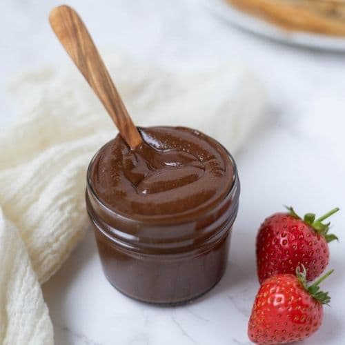 Close up of a jar of homemade Nutella on counter next to strawberries for dipping.