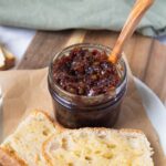 A jar of bacon jam with a wooden spoon ready to spread on sourdough toast.