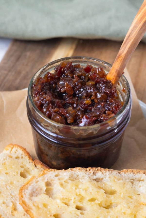 A jar of bacon jam with a wooden spoon ready to spread on sourdough toast.