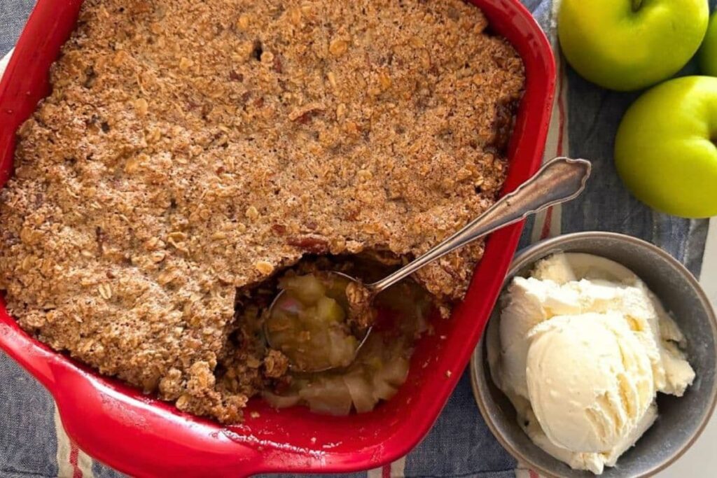 Sourdough apple crisp with a scoop taken out in a baking pan next to a bowl of ice cream.