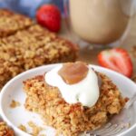 A slice of sourdough baked oatmeal on a plate topped with yogurt and apple butter for serving.