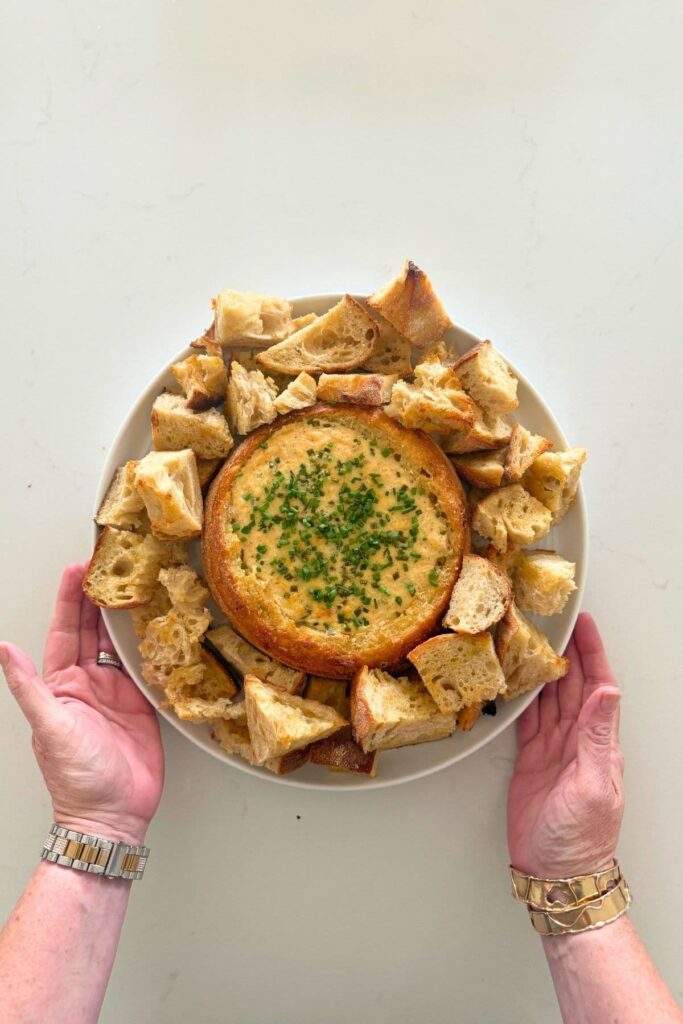 Adding toasted bread to a serving plate with a sourdough cheese and garlic cobb loaf dip for serving.