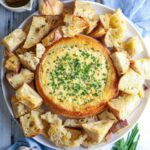 A sourdough cheese and garlic cobb loaf dip on a serving plate with toasted bread for dipping.