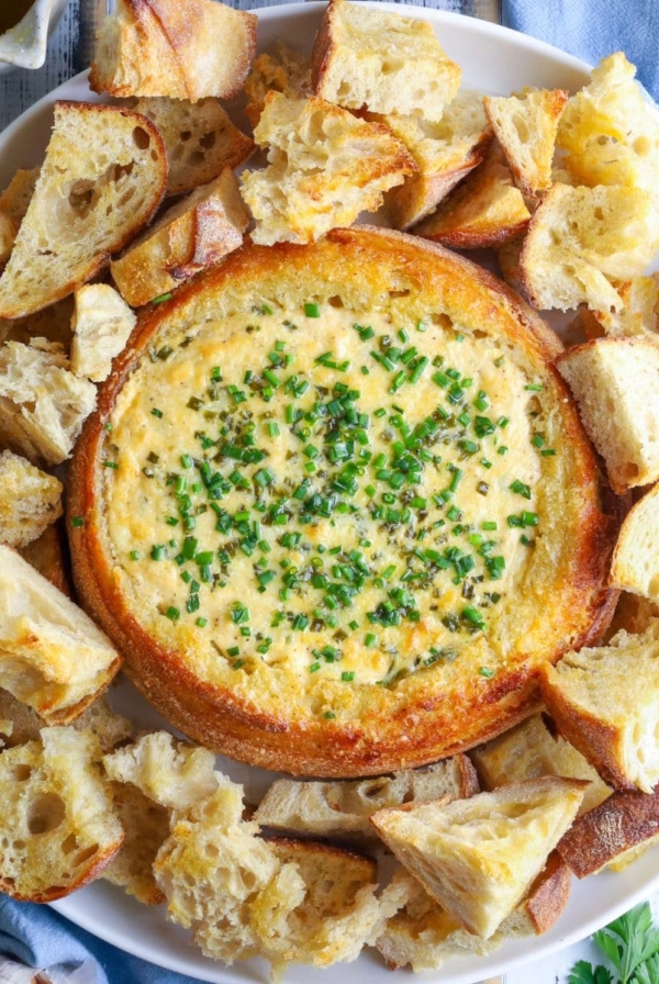 A sourdough cheese and garlic cobb loaf dip on a serving plate with toasted bread for dipping.