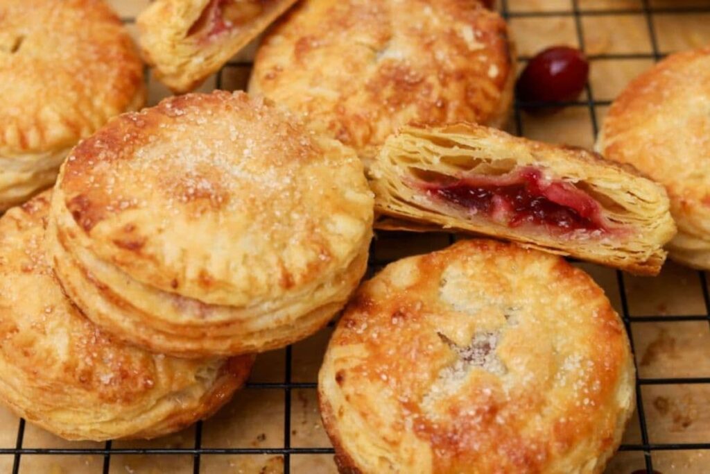 Close up of sourdough cranberry apple hand pies on a cooling rack with one split open to show inside texture.