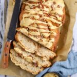 An overhead view of a sourdough maple pecan twist loaf with glaze topping and three slices sliced to show inside texture.