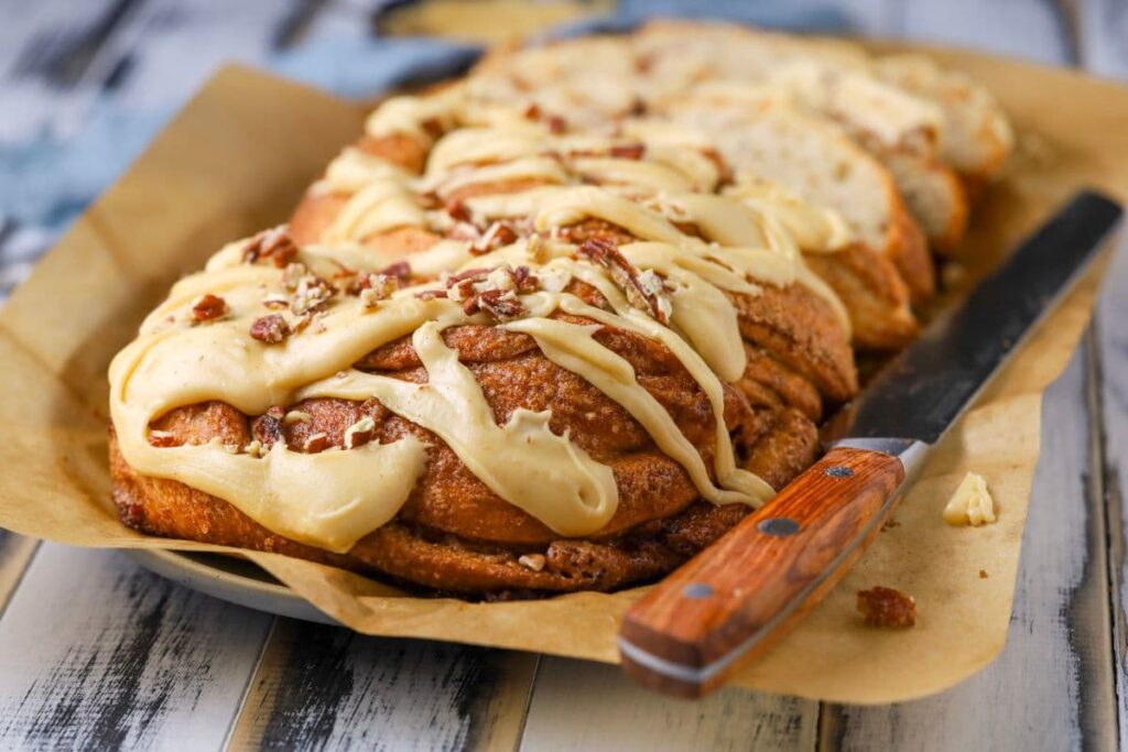 Close up of a sourdough maple pecan twist loaf on a piece of parchment paper with glaze on top.