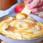 Hand dipping an apple slice into a bowl of whipped caramel dip.