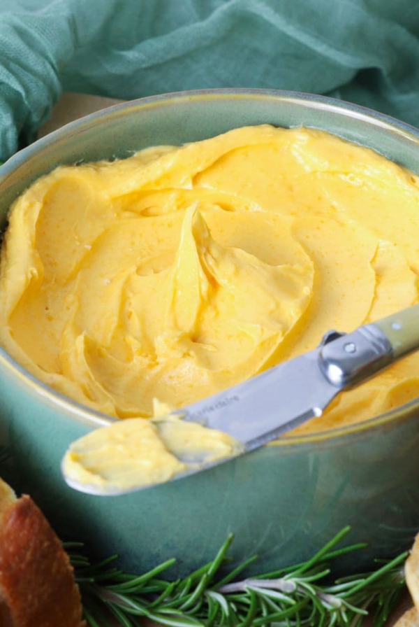 Close up of cheddar butter in a serving bowl with a butter knife for spreading onto bread.