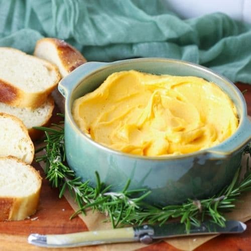 Cheddar butter being served in a bowl on a serving board with slices of sourdough bread.