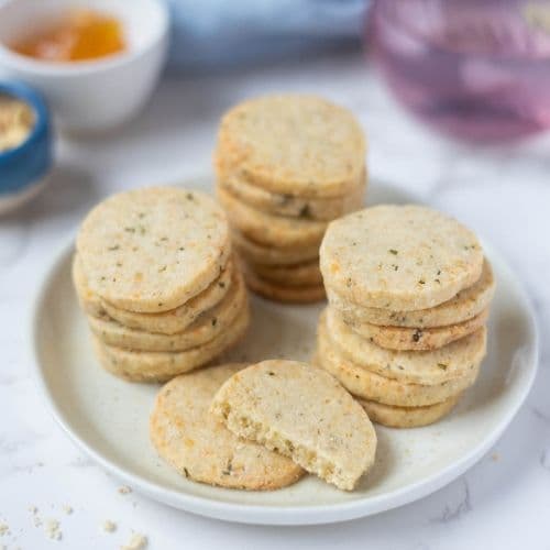 Stacked sourdough discard rosemary and parmesan shortbread biscuits on a serving plate with one broken in half to show texture.