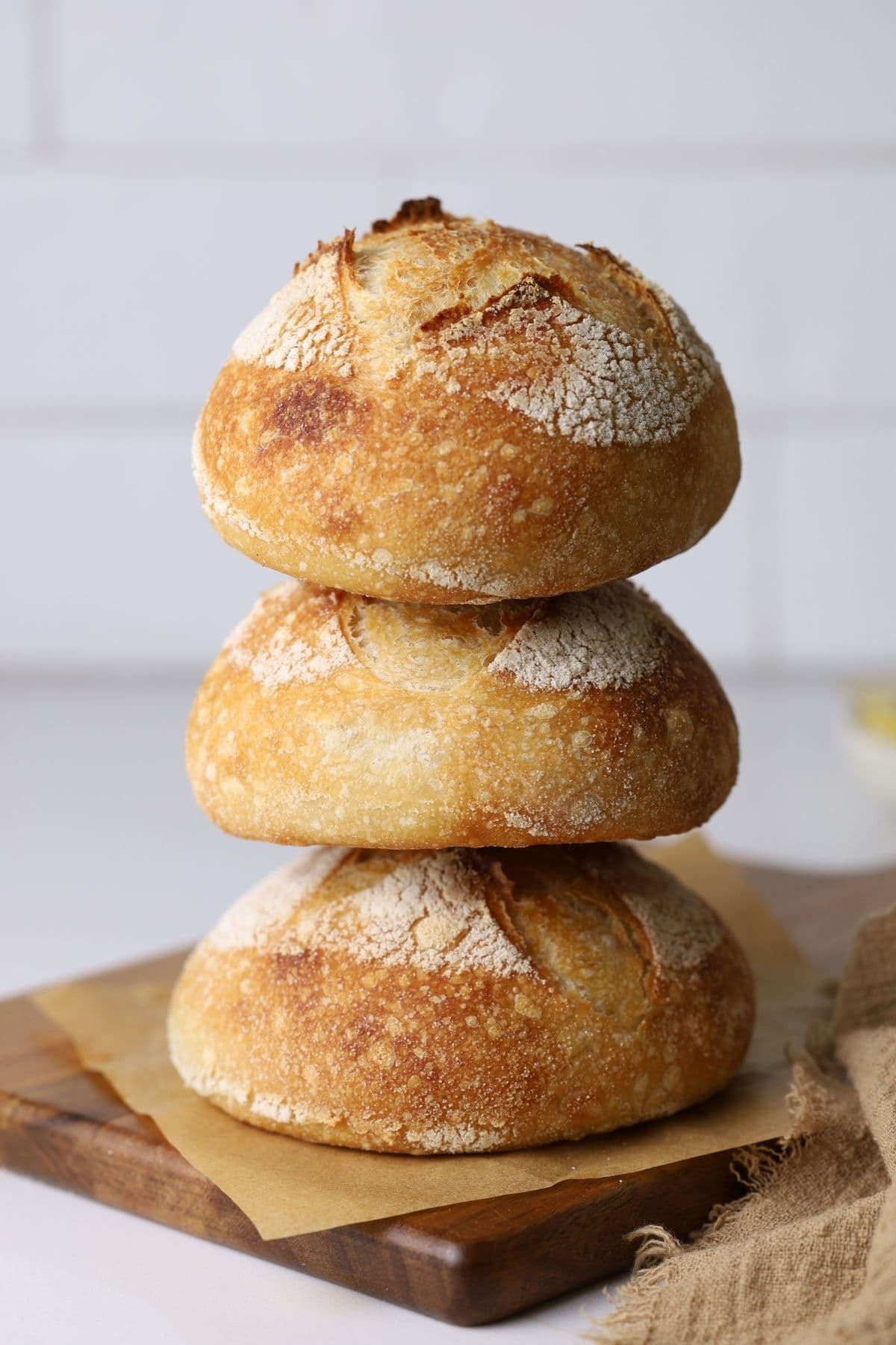 Three mini sourdough boules stacked on a piece of parchment paper on a serving board.