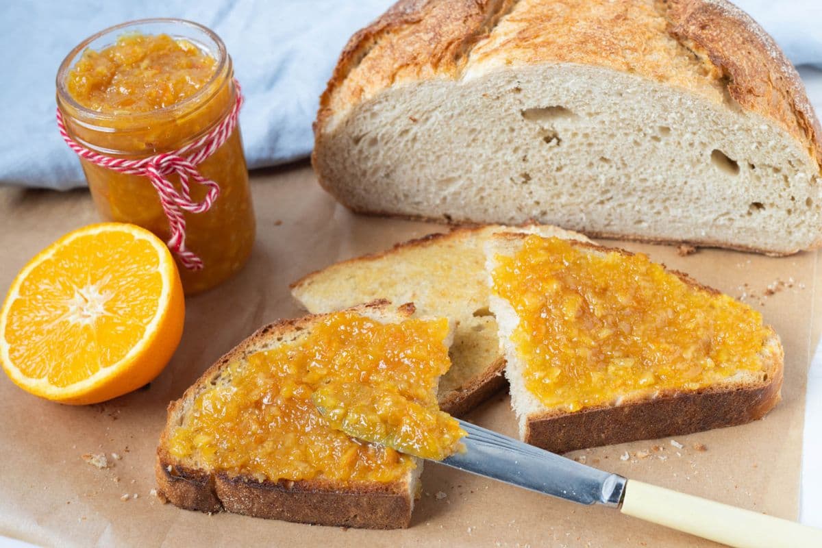 A slice of sourdough bread next to the full loaf, topped with a fresh batch of shortcut orange marmalade.