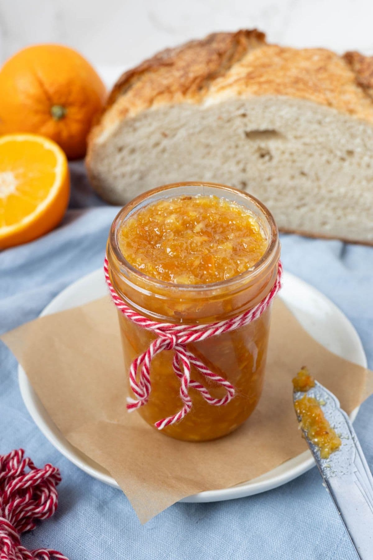 A jar of shortcut orange marmalade on a plate on the counter, ready for serving with sourdough bread.
