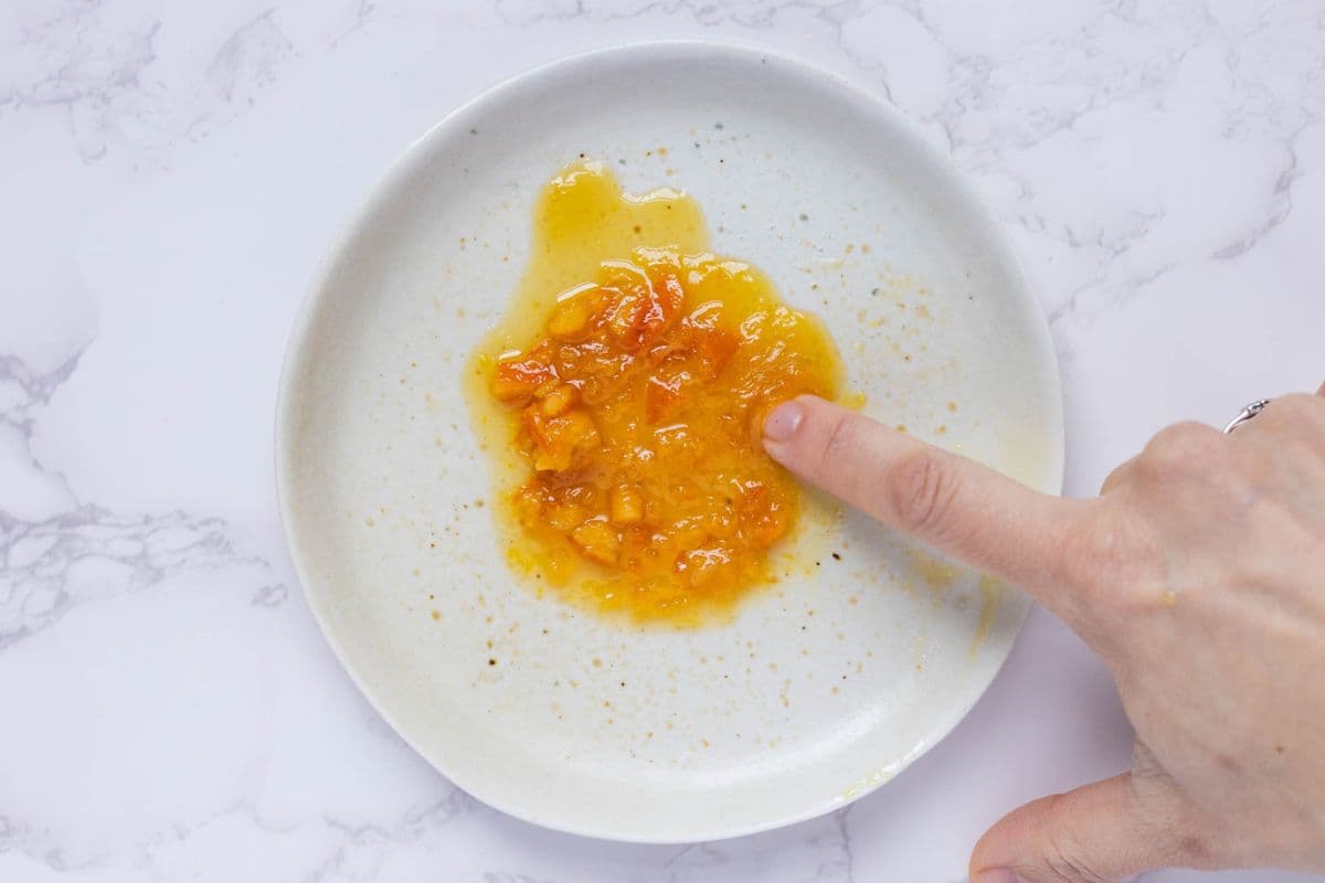 Checking for doneness of the marmalade by performing the plate test with a scoop of shortcut orange marmalade on a cold plate.