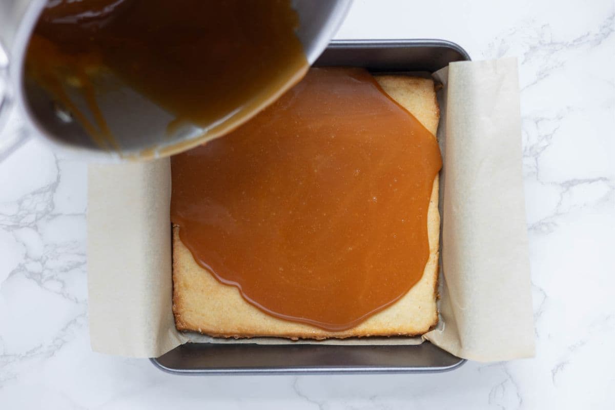 Pouring homemade caramel sauce over baked shortbread to make sourdough twix cookies.