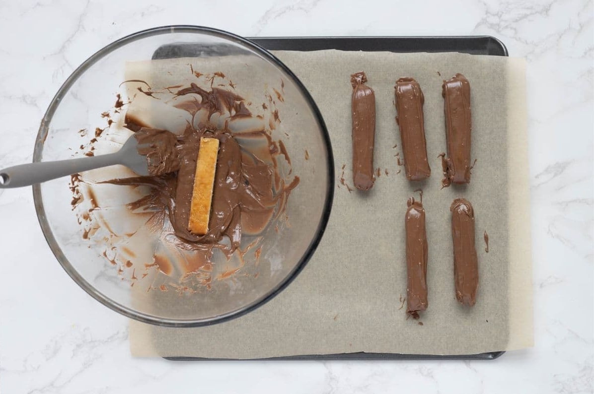 Dipping caramel coated shortbread bars into a bowl of melted chocolate to make sourdough twix cookies.