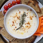 Close up of white bean dip topped with chili flakes and on a serving platter with sourdough toast and vegetables.