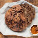 A loaf of chocolate sourdough discard bread on a cutting board, sliced for serving with jam.