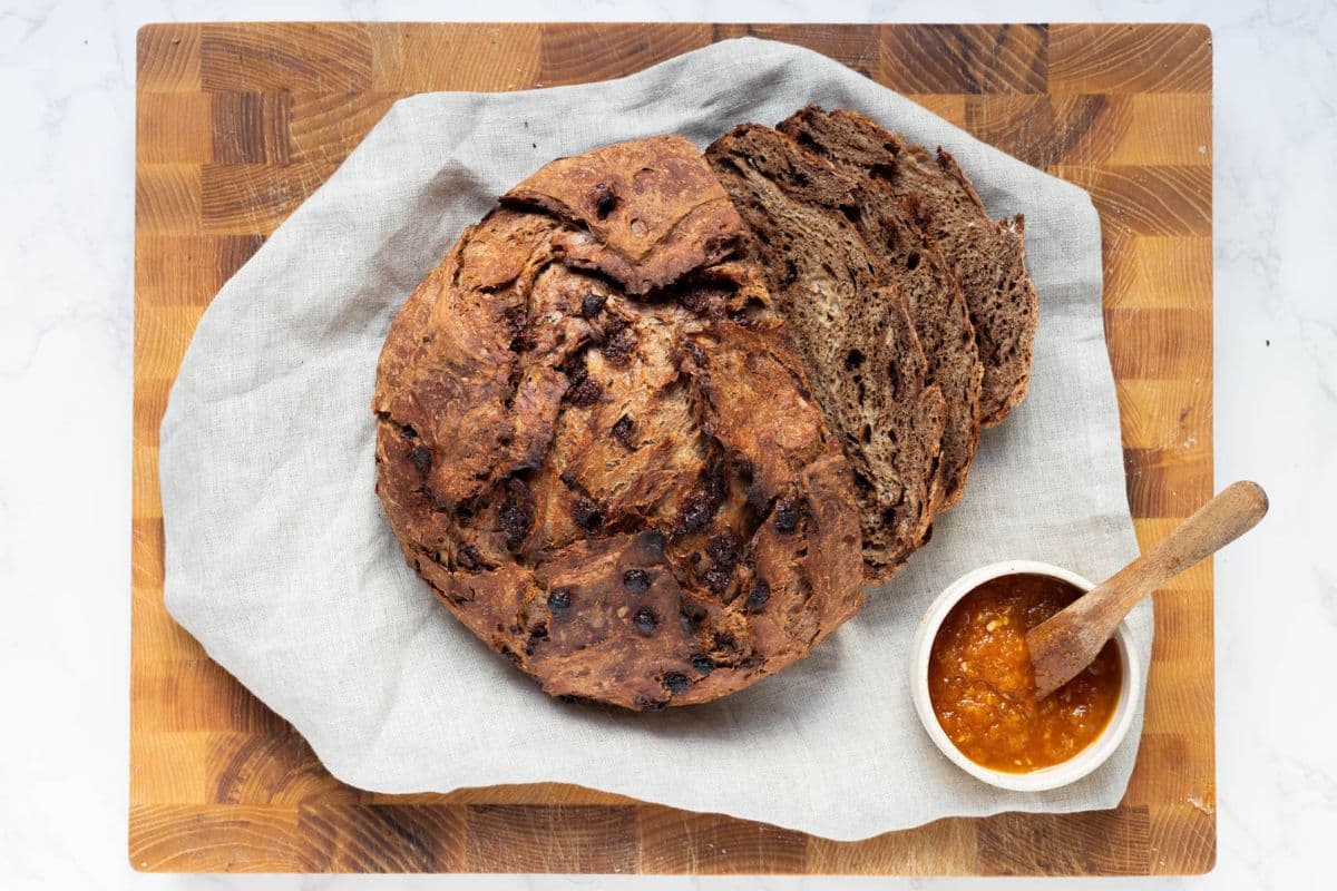 A load of chocolate sourdough discard bread on a cutting board with a bowl of jam for serving.