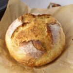 A crusty loaf of sourdough discard bread baked to golden perfection sitting on a piece of parchment paper.