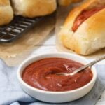 A bowl of homemade ketchup on the table with hot dogs for serving.