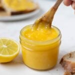 Scooping out lemon curd from a jar to add to toast.