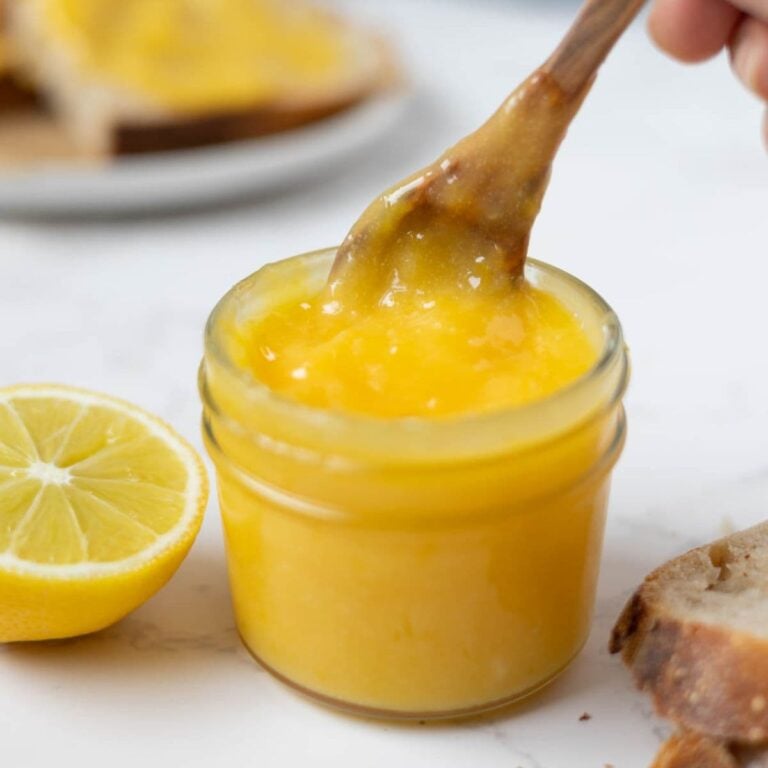 Scooping out lemon curd from a jar to add to toast.