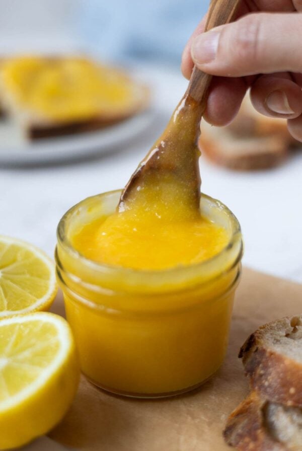 A wooden spoon scooping out lemon curd from a jar.