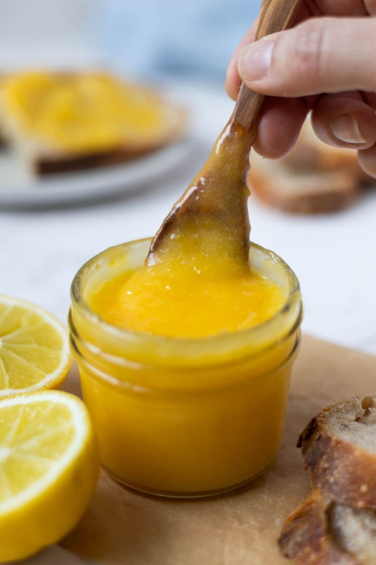 A wooden spoon scooping out lemon curd from a jar.