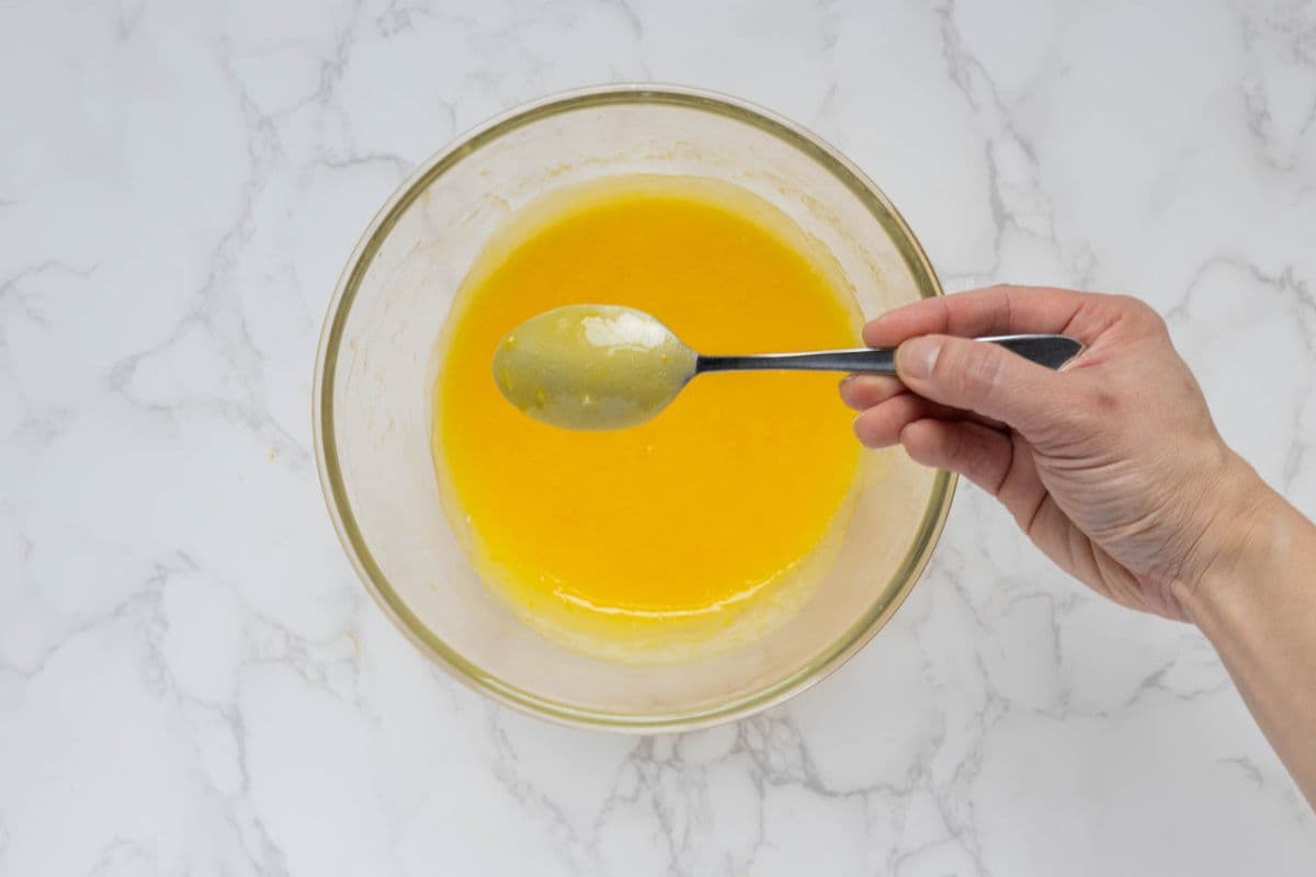 Showing the thickness of the finished lemon curd by dipping a spoon into mixture.