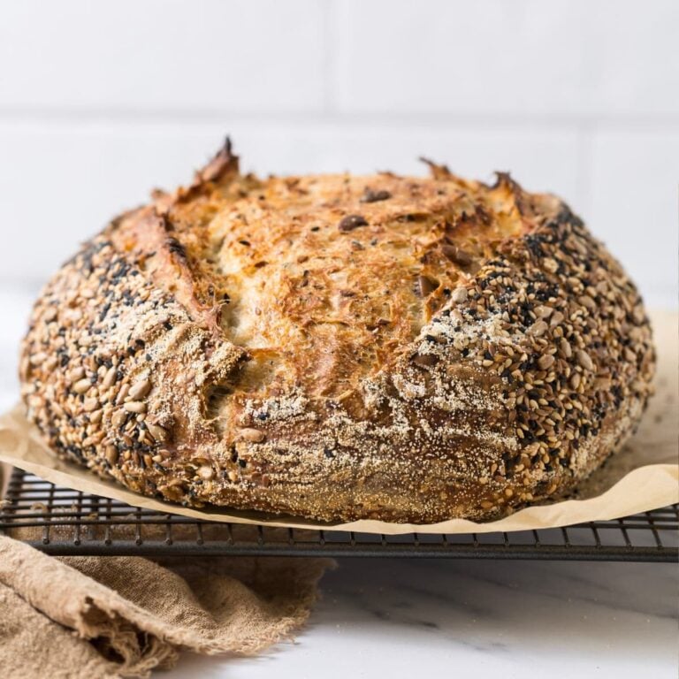 A loaf of multigrain sourdough bread on a parchment lined cooling rack.