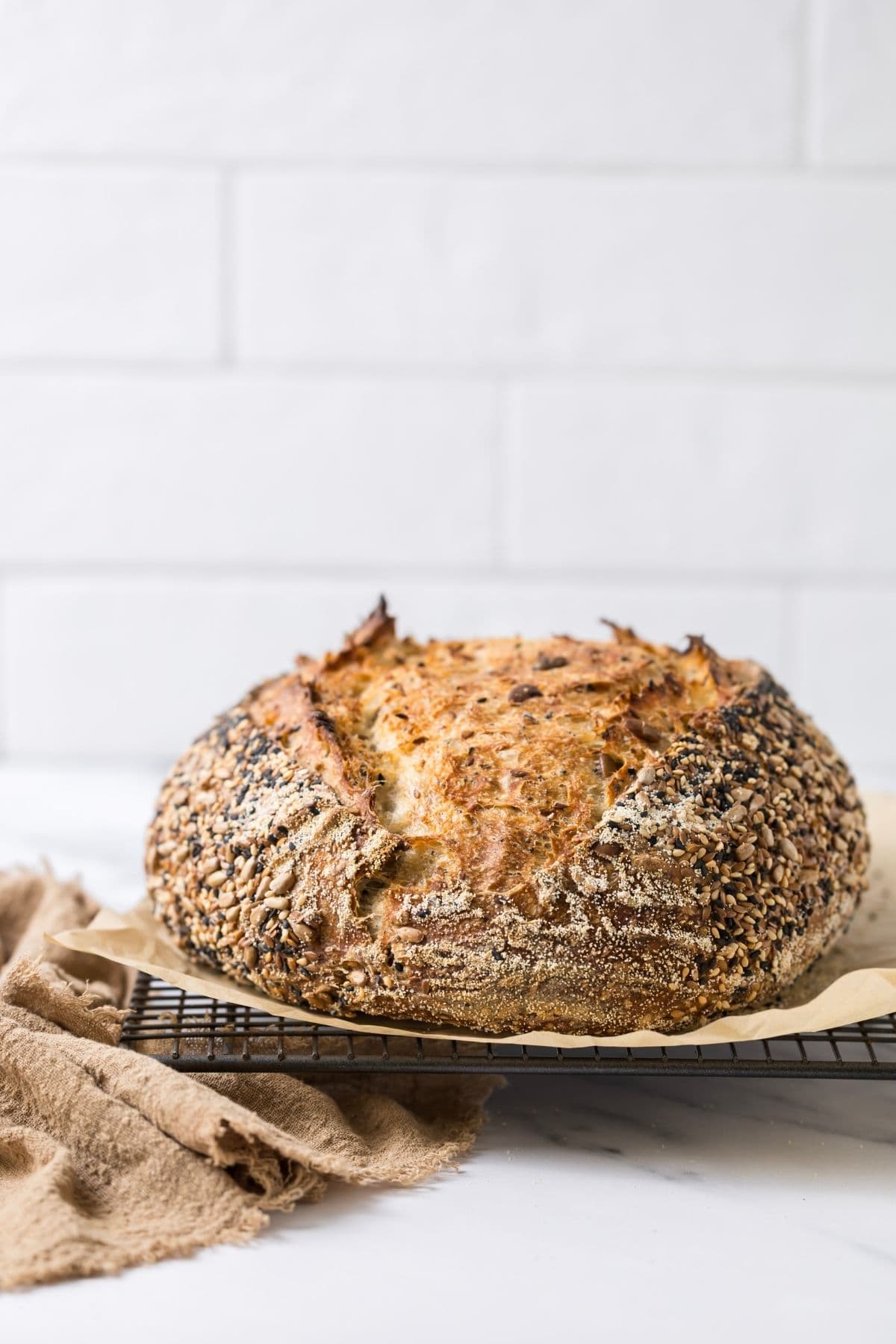 A whole loaf of fresh baked multigrain sourdough bread on a cooling rack.