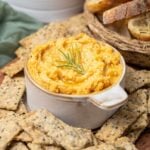 Close up of a bowl of potted cheese with a rosemary sprig on top.