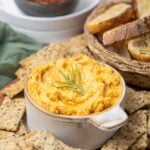 A bowl of potted cheese being served with seeded sourdough crackers and crostini for dipping.