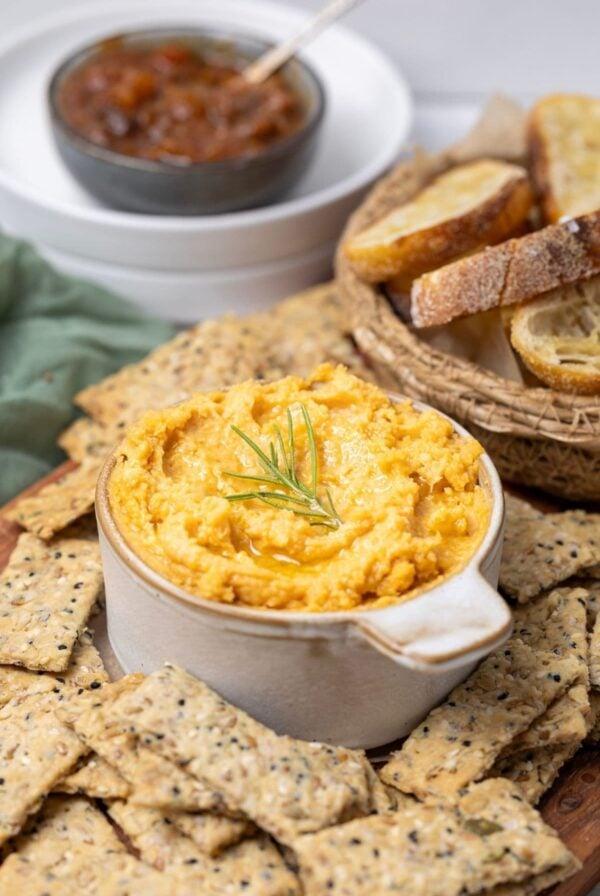 A bowl of potted cheese being served with seeded sourdough crackers and crostini for dipping.
