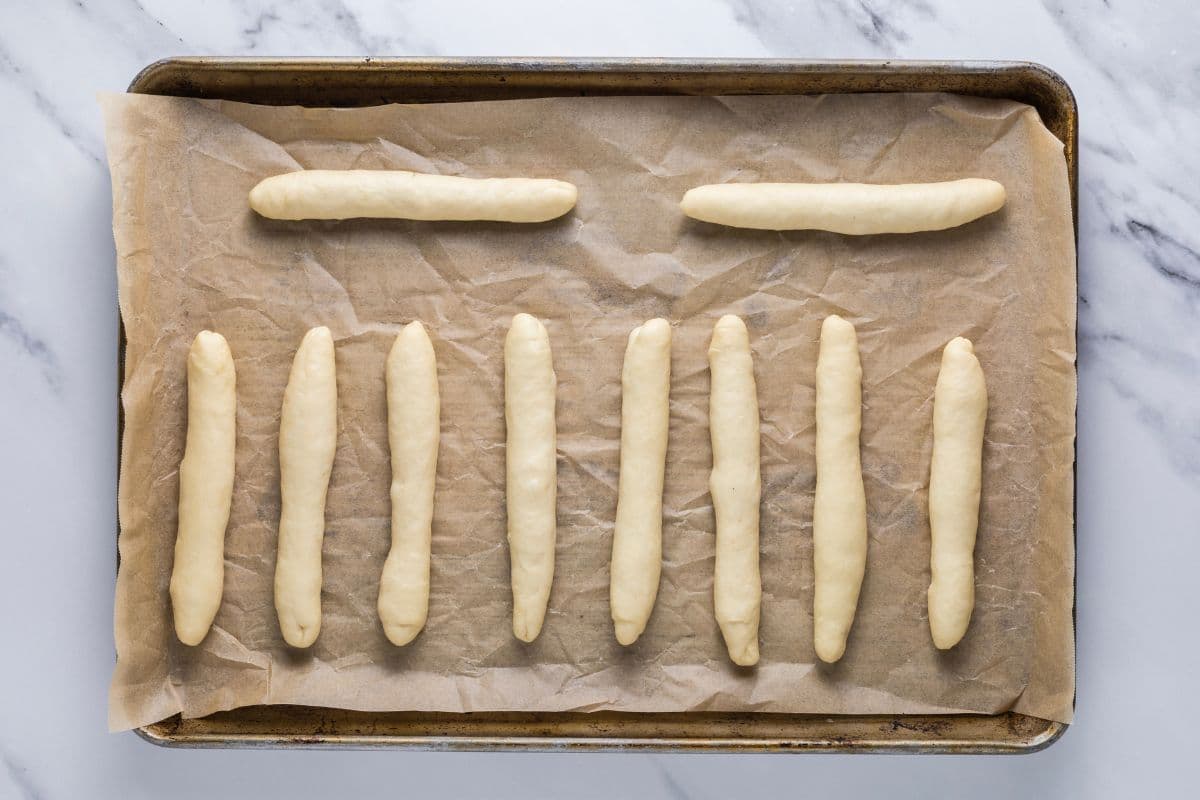 Soft sourdough breadstick dough on a parchment lined baking sheet ready to be placed in the oven.