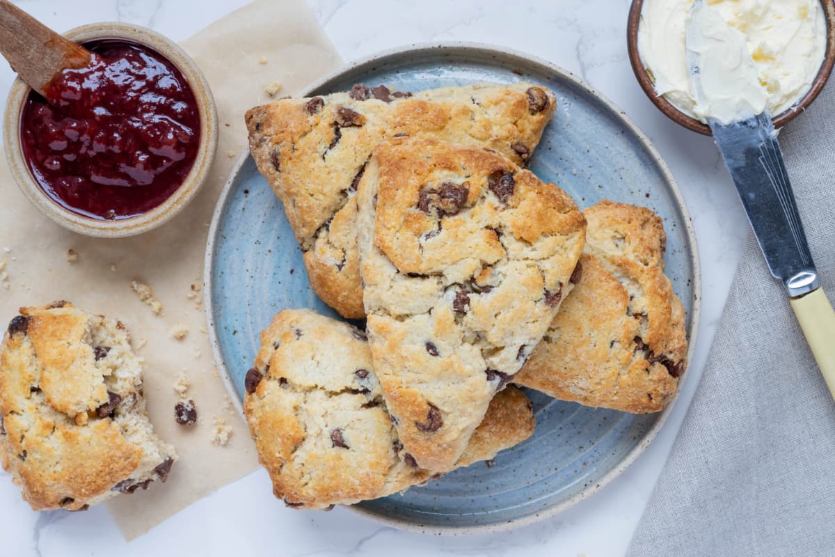 Overhead view of chocolate chip sourdough scones stacked on a small plate being served with jam and cream.